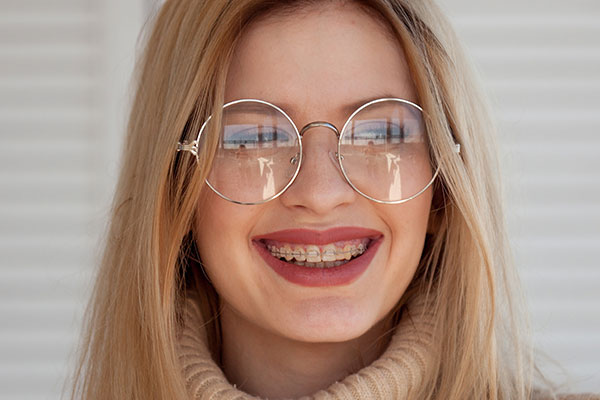 The image shows a woman with blonde hair, wearing glasses and a necklace, smiling at the camera.