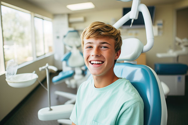 A young man is seated in a dental chair, smiling broadly.