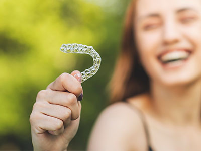 A smiling woman holding a transparent dental retainer in her hand.